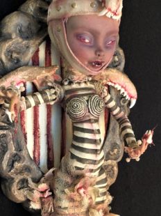 mixed media artpiece mounted on wooden board gothic dark circus-themed toothfairy doll wearing black and white stripes and animal jawbone for a headdress, jawbones for wings