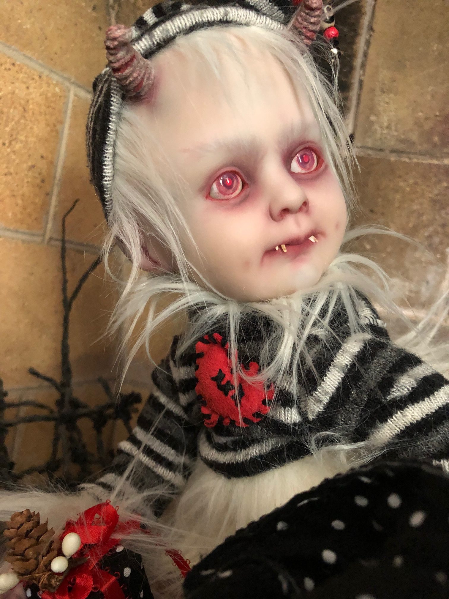 creepy baby holiday elf doll with red eyes, white hair and fur dressed in gray, black and white stripes with horns