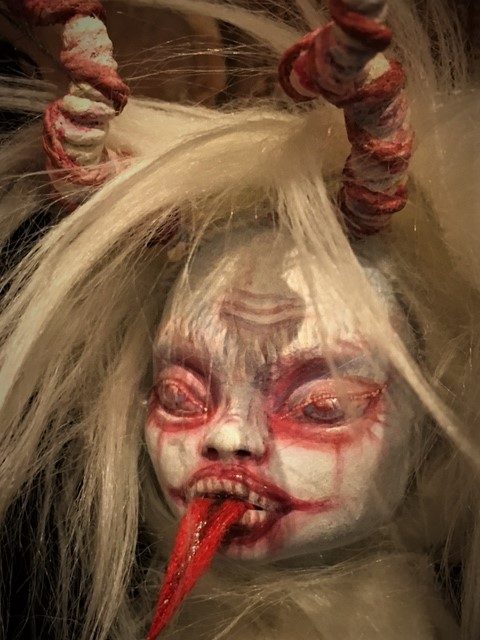close up of a white albino krampus doll face sticking out his tongue and leering
