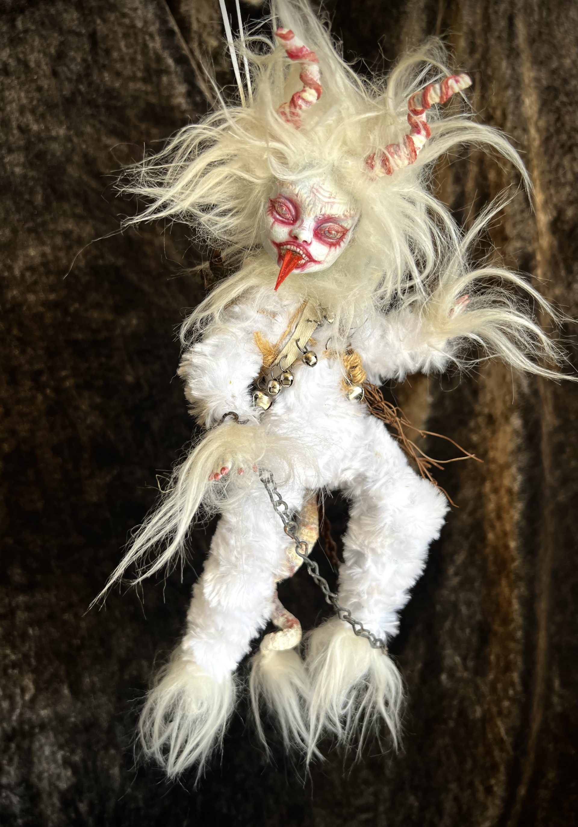 leering white albino krampus art doll with his tonue out white hair and fur, horned, chains