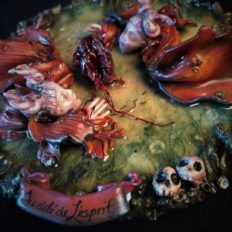 resin encased mixed media assemblage of two doll-faced orange fish rising out of the water to see a beating heart with little skulls