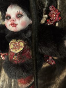 close-up gothic art doll with black fur long eye lashes and red makeup wearing hand-painted devil pendant