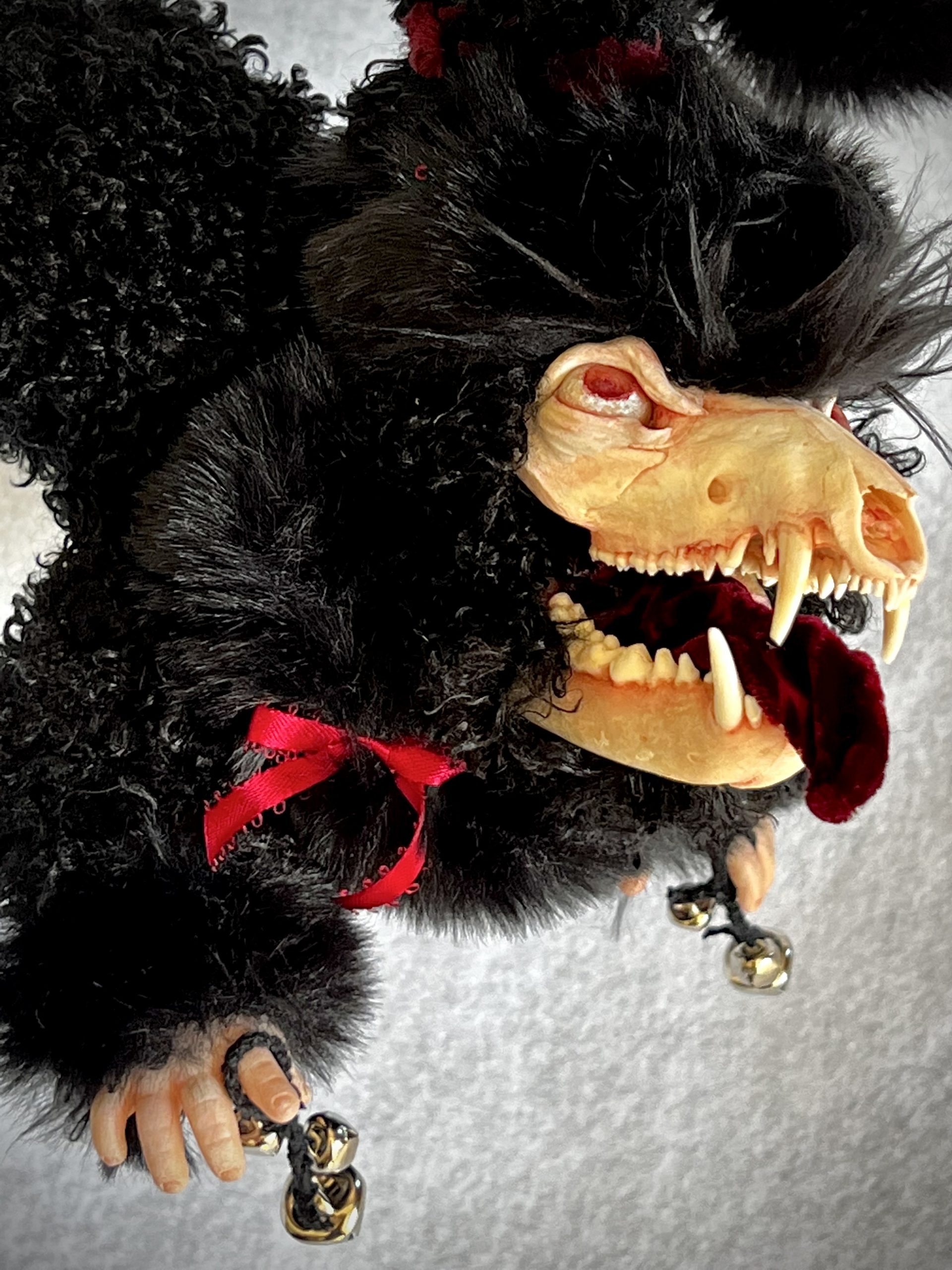 close-up hanging furry black creature with a hand painted coyote skull holding holiday bells