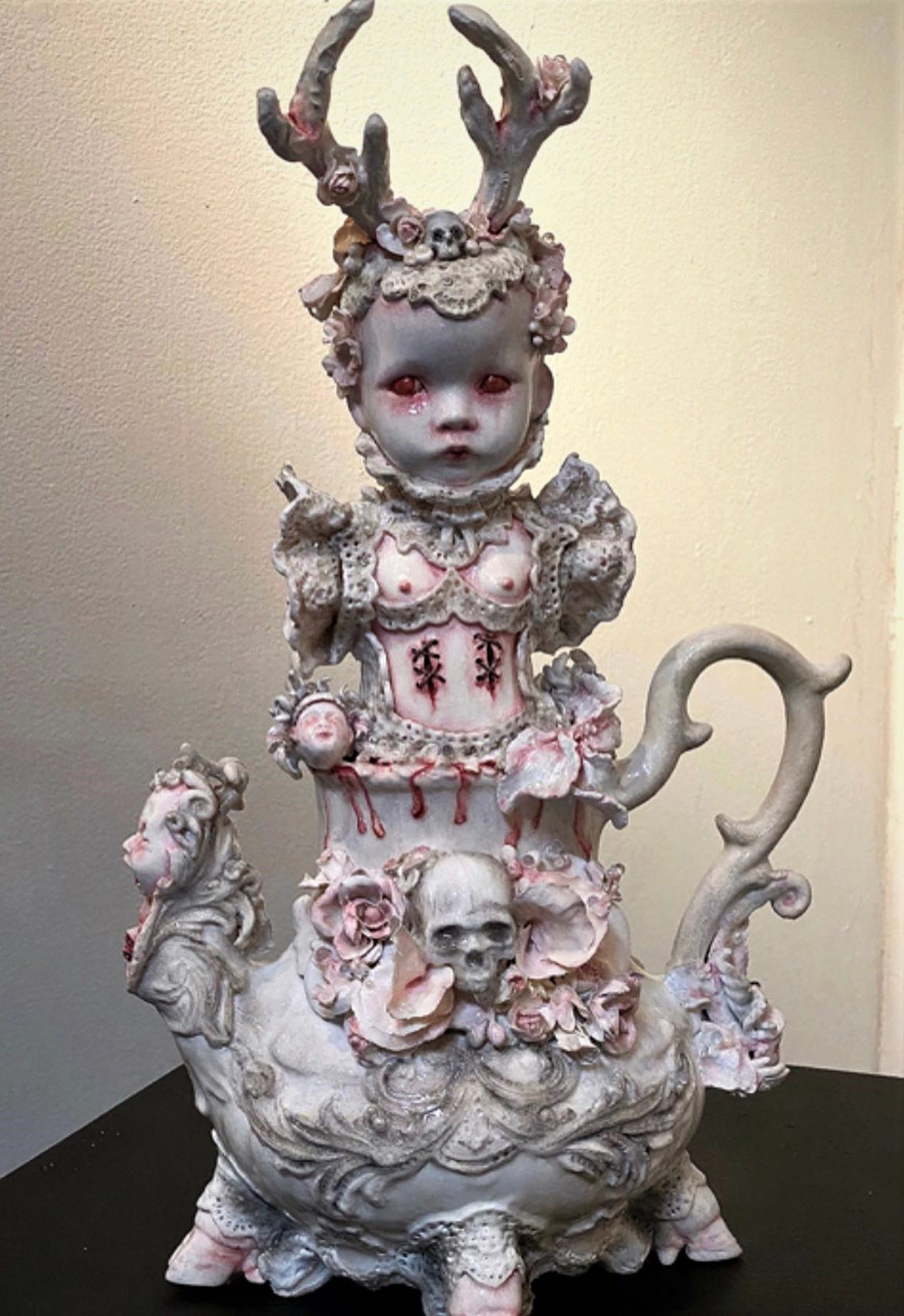 white mixed media assemblage teapot with a babydoll head wearing an antlered headdress
