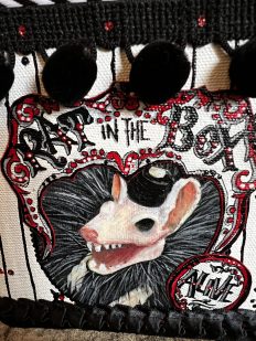 a close-up of hand-painted illustration of a skull faced rat wearing a beret gothic black white and red with black pom poms