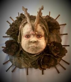 mixed media assemblage plaque repainted babydoll head with a jaw bone headdress and flowers and nails mounted on wood