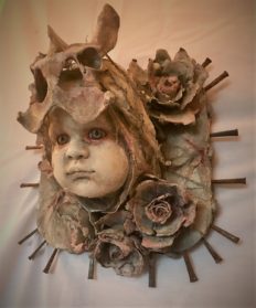 mixed media assemblage plaque repainted babydoll head with a bone headdress and flowers and nails mounted on wood