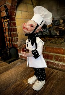 sideview close-up hand painted vinyl pig doll wearing chef uniform holding bloody heart