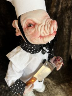 close-up hand painted vinyl pig doll wearing chef uniform holding bloody heart and cleaver