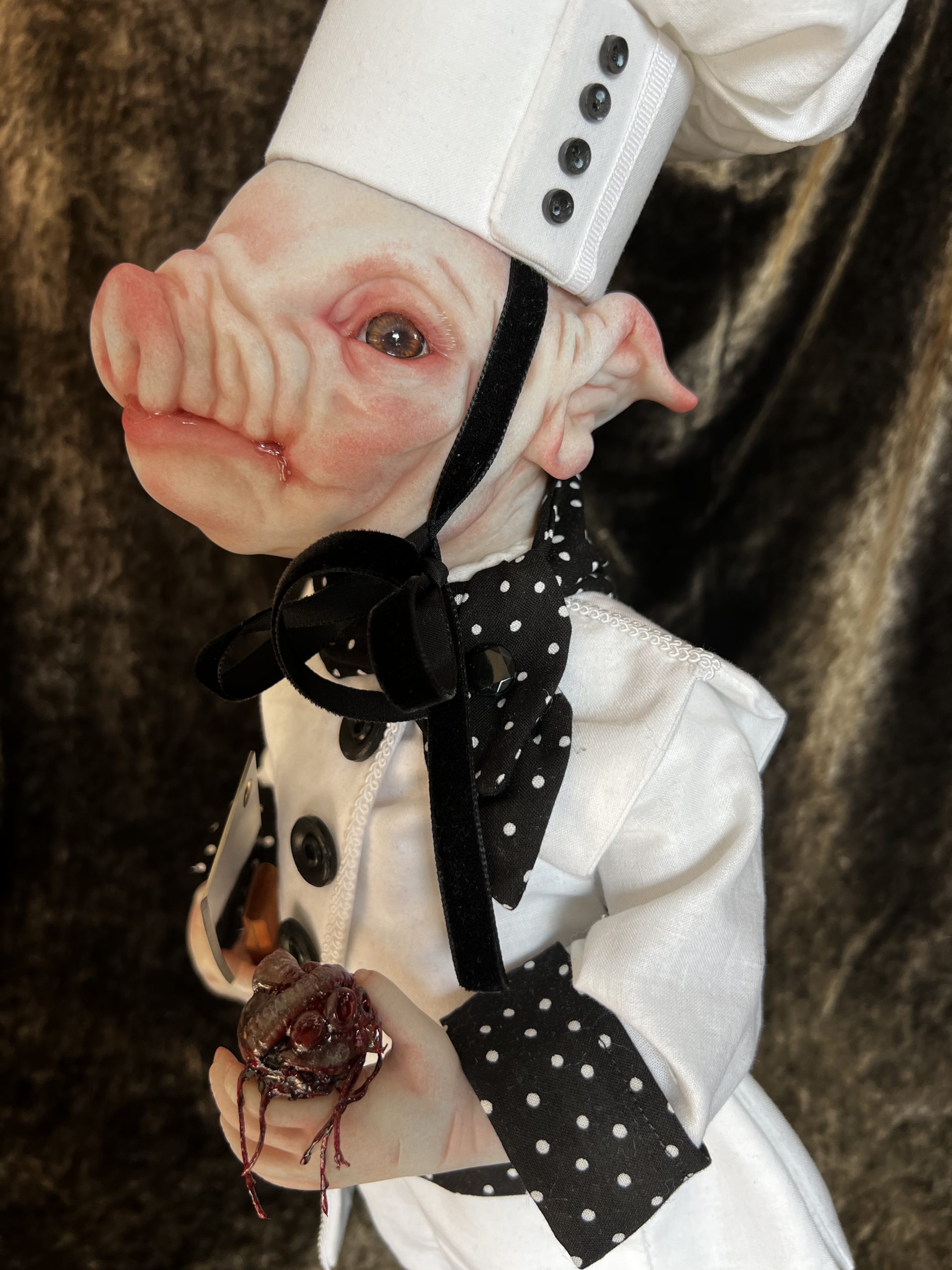 close-up hand painted vinyl pig doll wearing chef uniform holding bloody heart