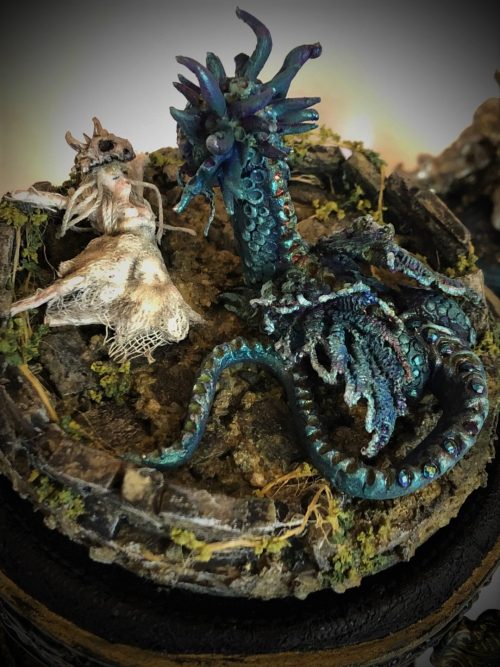 blue and green sculpted fantasy dragon above lifeless maiden on a platform