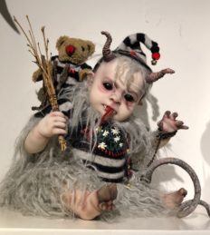 mixed media artdoll creepy evil babydoll elf with horns, black eyeballs, pointed elf ears, tongue sticks out, faux fur collar, striped cap and sweater, cloven hoof foot, curly tail, faux fur legs and teddy bear on his back