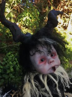 close up of Krampus gothic artdoll face black horns, black and white hair, red rimmed eyes tongue out