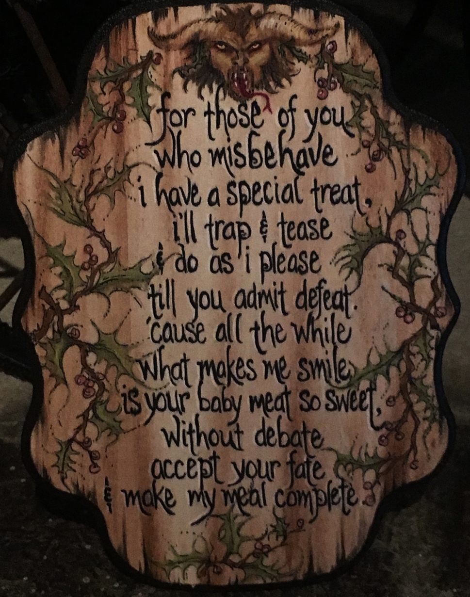 hand painted lettered poem on wooden sign with krampus head