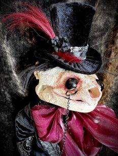 close-up of art doll with head made of a turtle skull wearing velvet top hat and jacket, monocle
