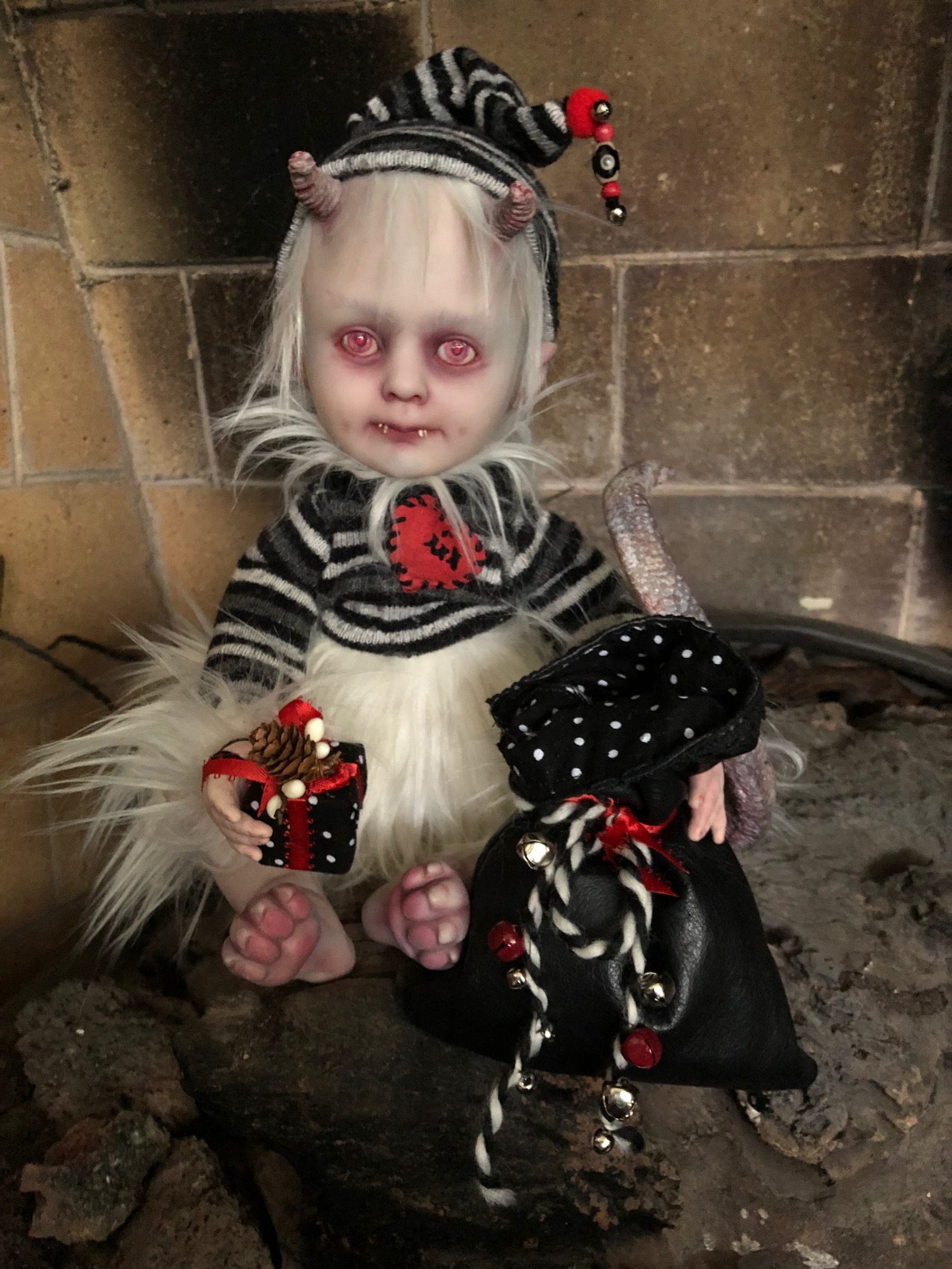 creepy baby holiday elf doll with red eyes white hair and fur dressed in stripes with horns, canine paws, and a reptilian tail.