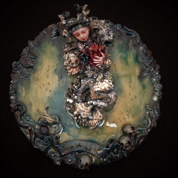 resin encased mixed media assemblage of a doll-faced lion fish creature holding a skull and a heart on board