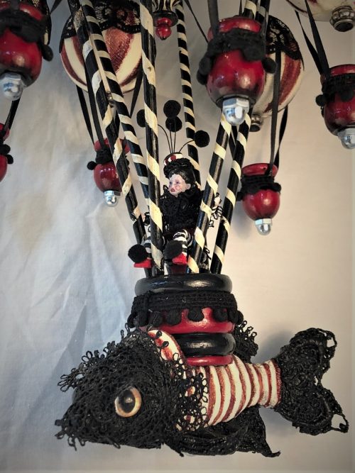 close-up red, black and white mixed media mobile striped miniature gothic circus performer rides a hot air balloon with a lace-covered koi fish