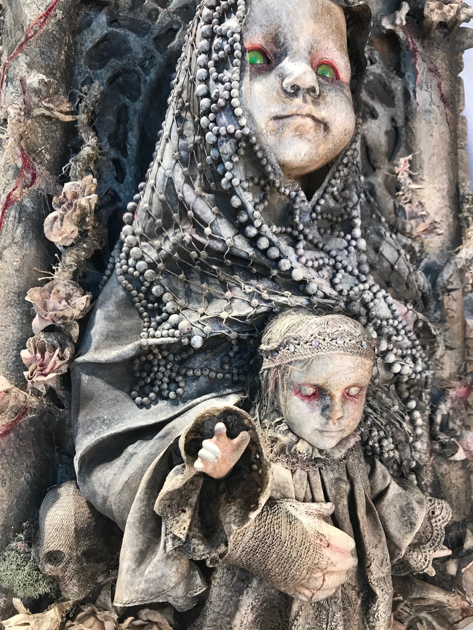 close up mixed media assemblage plaque repainted sainted robed baby doll holding a baby