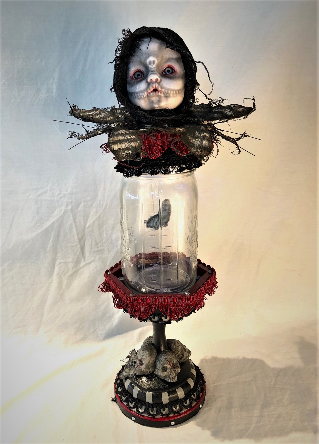 mixed media assemblage gothic day of the dead skeleton babydoll head repaint on top of mason jar holding toy moth on skull-adorned pedestal