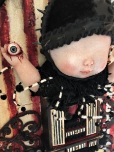 close-up red, white and black striped mixed media gothic circus-themed artpiece of a doll holding her own bloody eyeballs with a small cabinet holding a heart for her torso