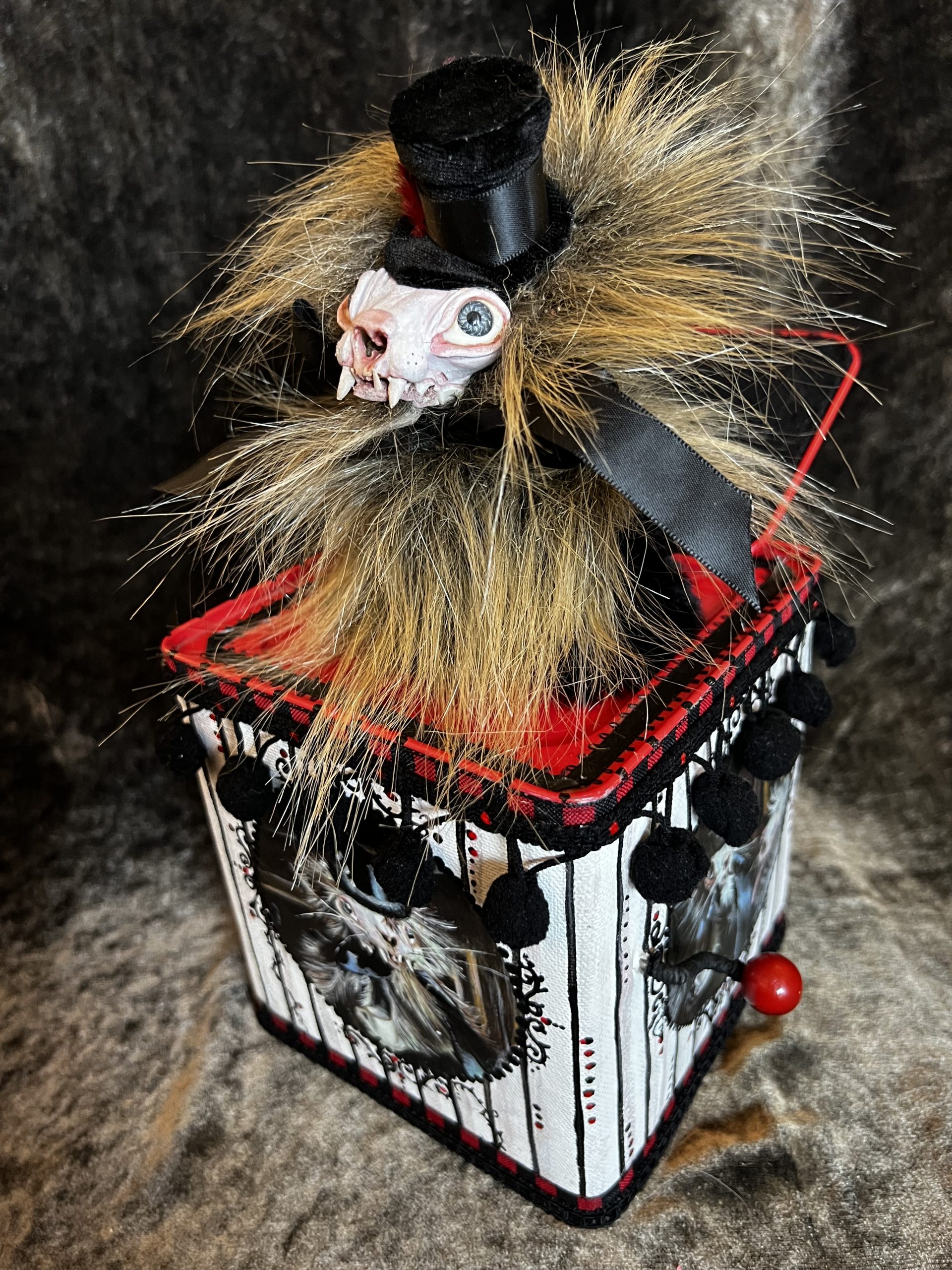 hand-painted gothic mixed media jack in the box assemblage with a furry skull-faced weasel wearing a top hat and box