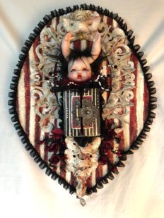 gothic red black and white mixed media assemblage artpiece plaque with a repaint porcelain babydoll head with arms for horns, striped closed cabinet, vertebrae, surrounded by wishbones on a painted wooden board