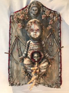 mixed media assemblage plaque bloody mummified babydoll with skeleton wings and a skull in the stomach