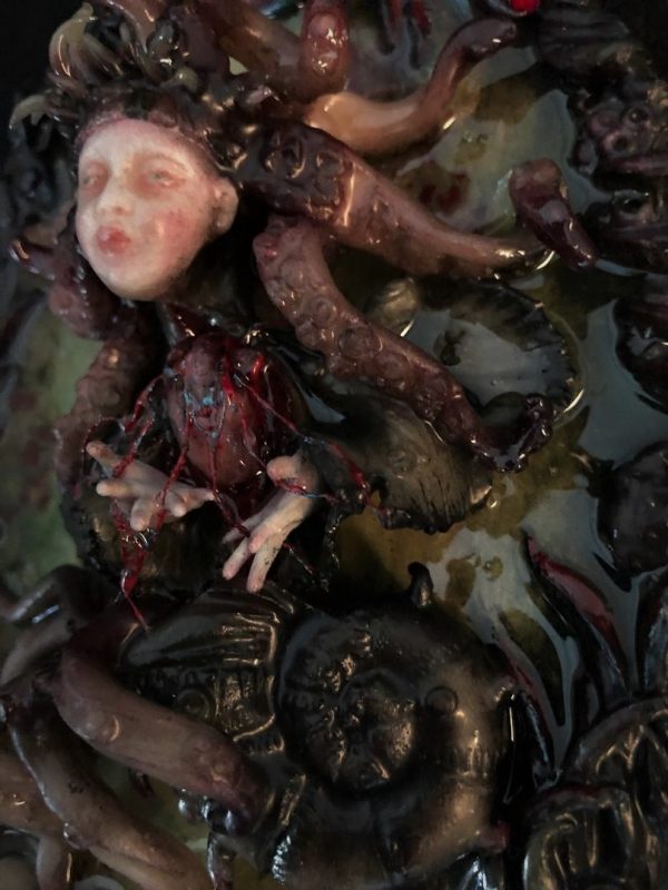 close-up of resin encased mixed media assemblage of a tiny tentacled, doll-faced creature floating in water holding a beating heart.