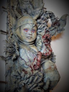 close-up of mixed media assemblage ghastly repainted baby dolls mounted on wooden board dark art