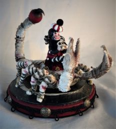 miniature gothic circus performer dressed in black white and red stripes rides a lace-covered scorpion on a painted wooden platform
