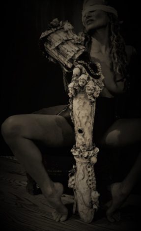 black and white photo of artist Stefanie Vega blindfolded behind a piece of her work made from an artificial leg