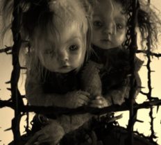 two art dolls huddled in a black thorn cage