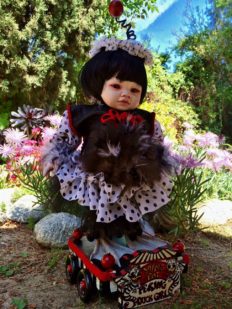 Asian Chinese girl doll with black bob wearing black and white polka-dot dress has feathers and taxidermy bird webbed duck feet standing on hand-painted wooden circus cart