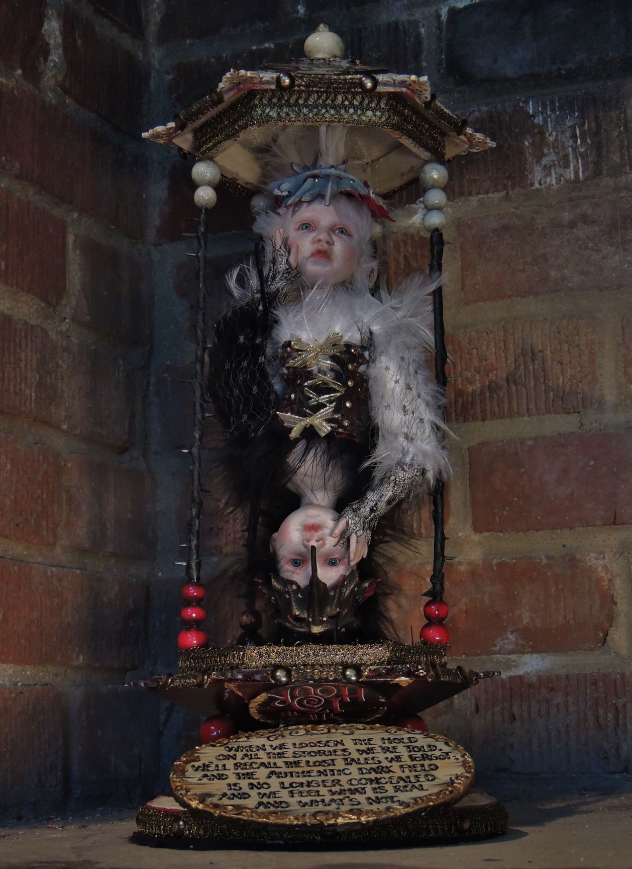 mixed media hourglass assemblage with an art doll that can be flipped to favor either the dark or light doll on top and hand painted poem on board
