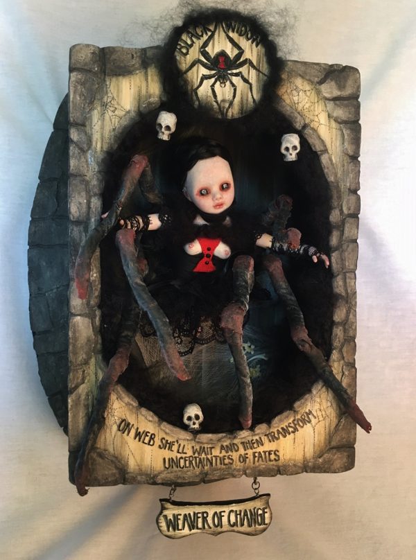 shadowbox mixed media assemblage of a gothic black widow themed doll with 8 legs pale with black hair and red hour glass she is inside a carved box with hand-painted wooden signs