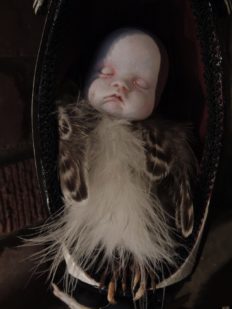 close-up sleeping baby doll with feathered bird body in an egg shaped containter