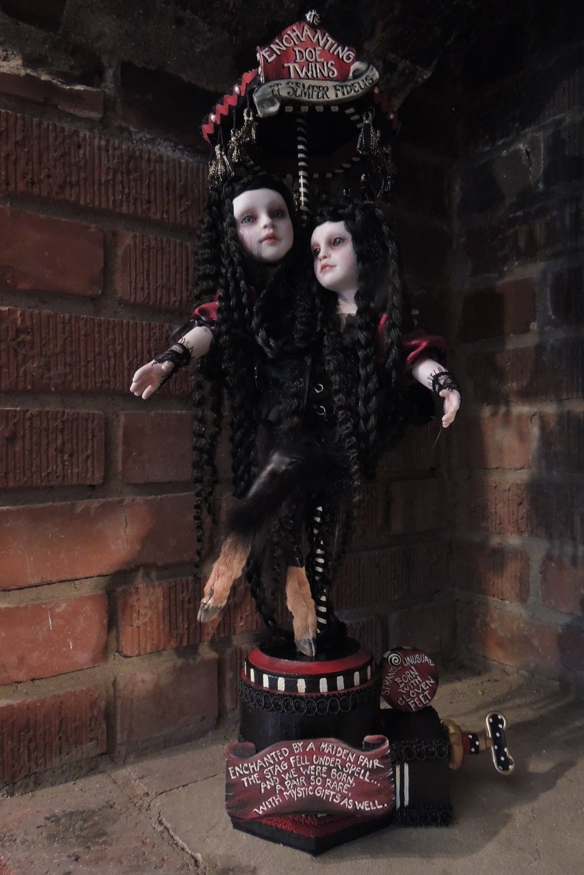 gothic conjoined twin artdolls with long crimped black hair and taxidermied deer doe feet on a pedestal music box with hand-painted signs