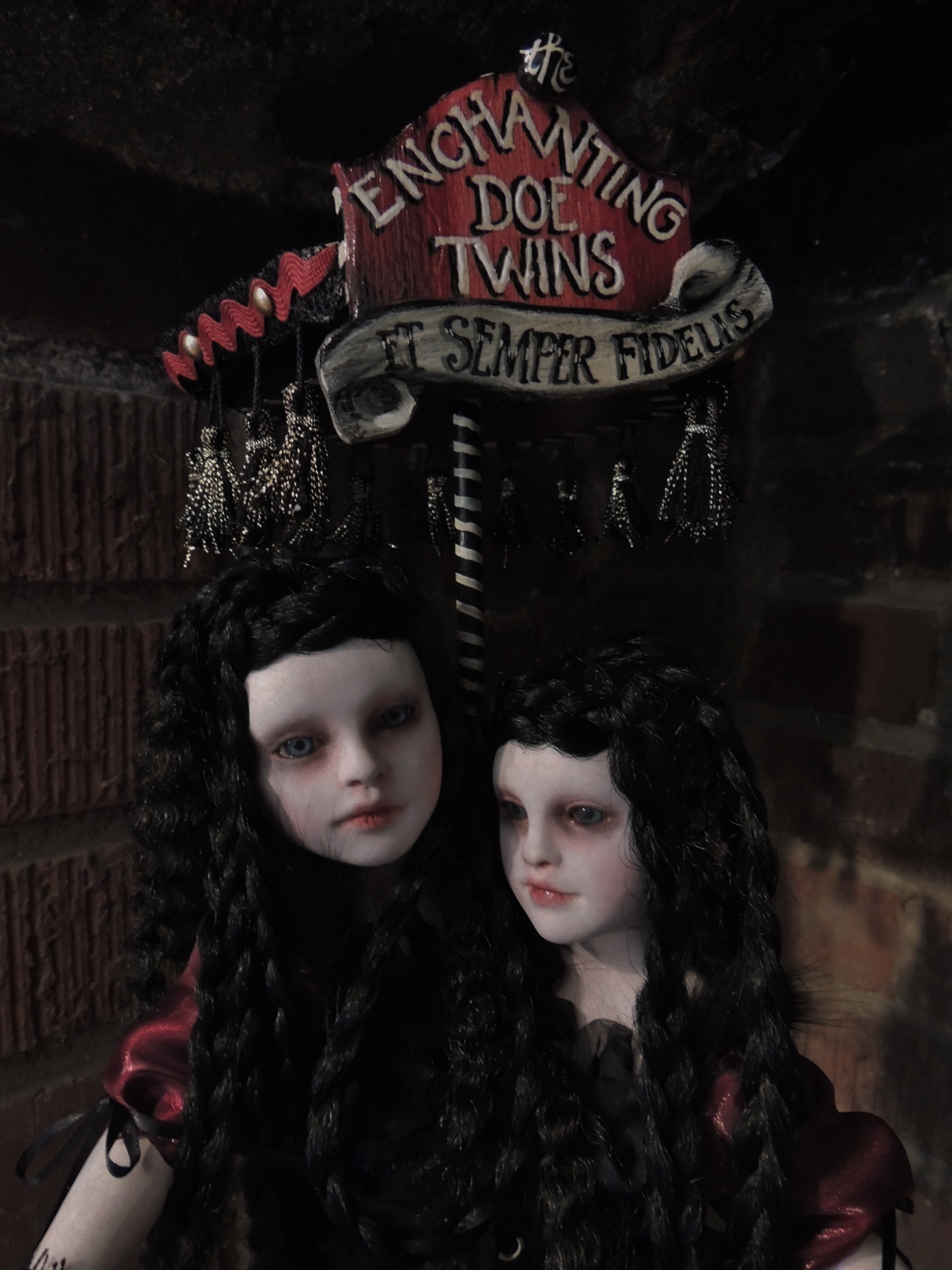close-up of gothic conjoined twin artdolls with long crimped black hair with hand-painted red and black sign