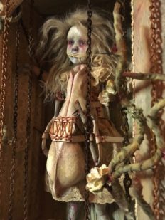close-up of mixed media assemblage shadow box earth tones with an imprisoned goth repainted doll.