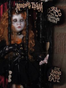 close-up gothic redheaded blind seer artdoll with taxidermy birdfeet trapped in a circus themed black thorny cage with hand-painted signs on it wall-mounted