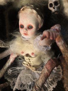 close-up of a ghostly gothic white spider themed doll with 8 legs pale with blond braided hair, red rimmed blue eyes, white corset and tutu