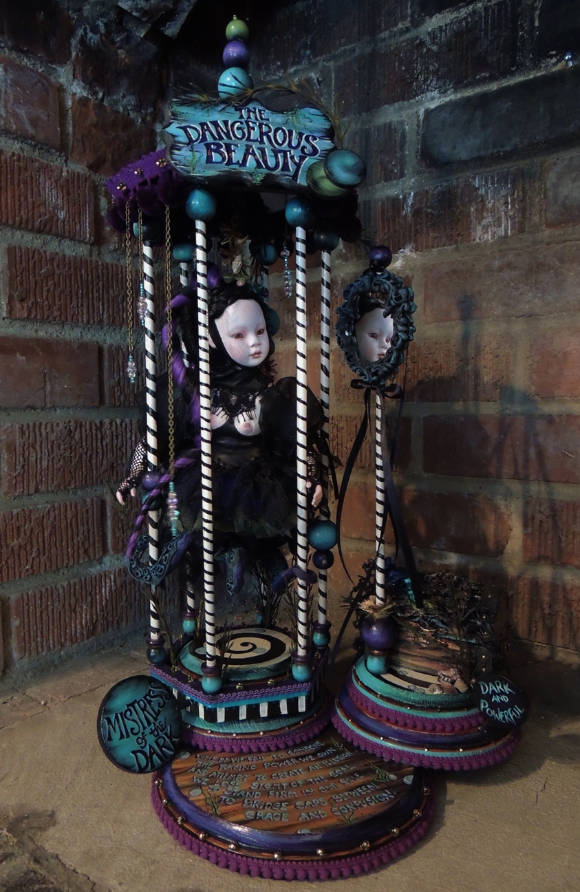 pale gothic artdoll wearing black with octopus tentacles looks at herself in a mirror inside a candy-coated blue and purple pedestal