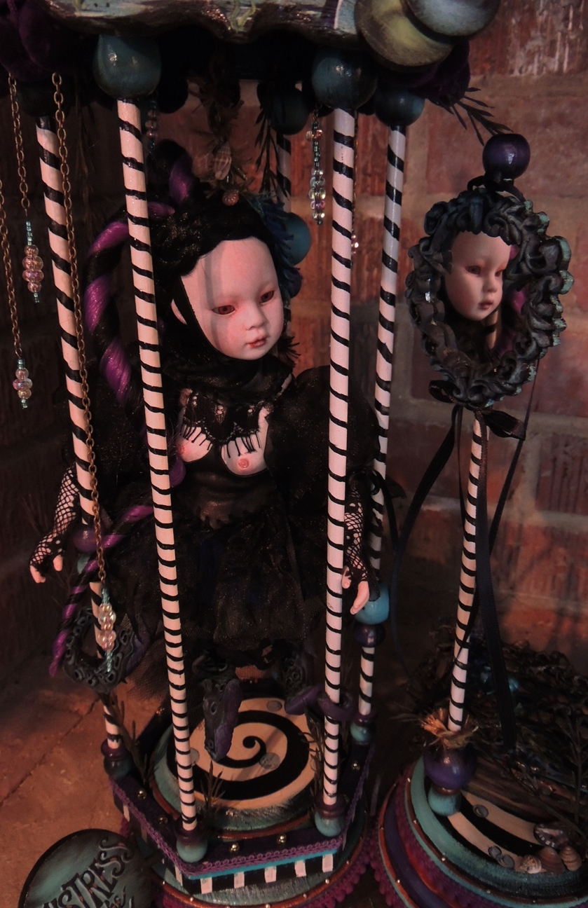 close-up of pale gothic artdoll wearing black with octopus tentacles looks at herself in a mirror inside a candy-coated blue and purple pedestal