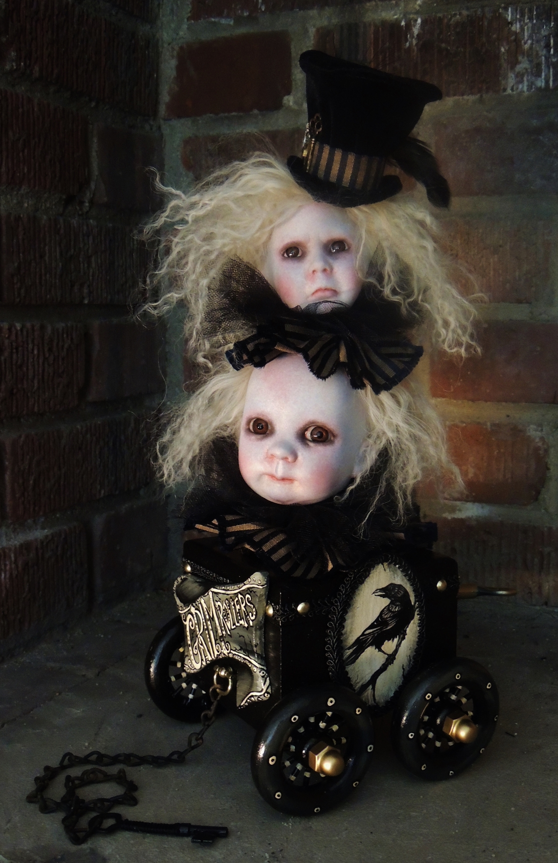 rolling pull-cart toy with a raven painted on the side and two gothic repainted doll heads with wild blond hair inspired by the works of the Brothers Grimm.