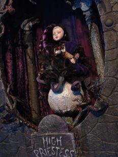 miniature shadowbox diorama with a tiny gothic artdoll purple and black with tentacles posed atop a sphere in a purple scene with columns