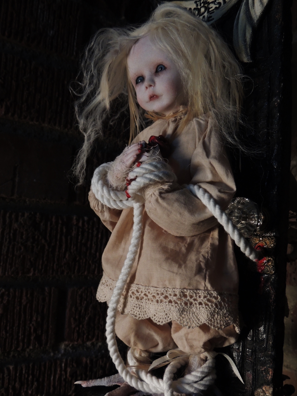 close-up of a gothic blond artdoll bound with rope to a carved wooden door