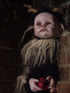 mixed media artdoll has hand-painted vinyl dollhead scrunched face with hand-sculpted horns, covered in black mohair fur, holds his heart in his hands