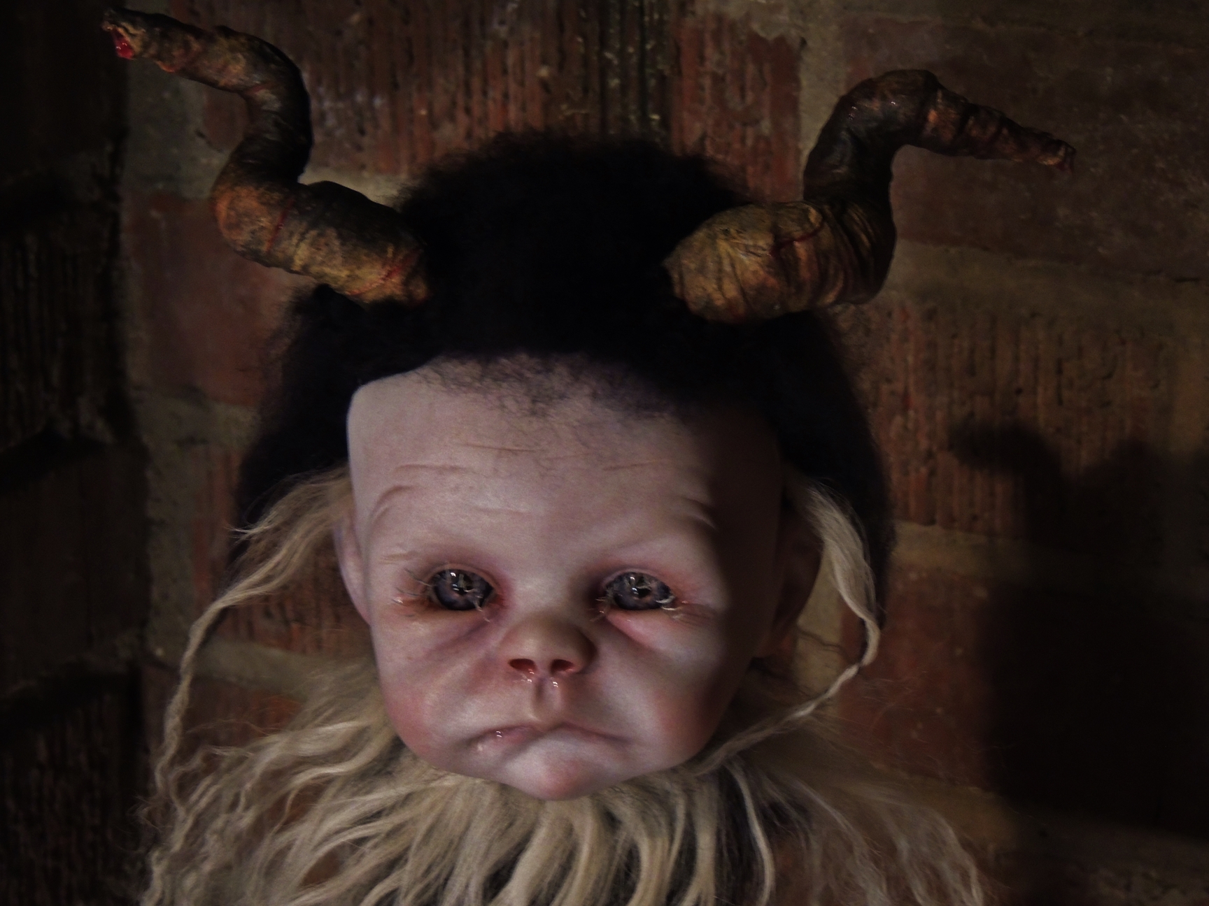 mixed media artdoll has hand-painted vinyl dollhead scrunched face with hand-sculpted horns, covered in black mohair fur