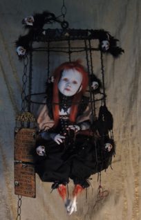 red headed goth doll taxidermy assemblage sitting in a black cage surrounded by seven raven birds